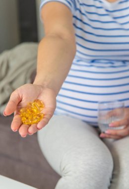 Hamile kadın omega üç içiyor. Seçici odaklanma. Beyaz.