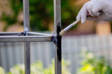 Bir adam metali siyah boyayla fırçayla boyuyor. Seçici odak