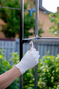 Bir adam metali siyah boyayla fırçayla boyuyor. Seçici odak