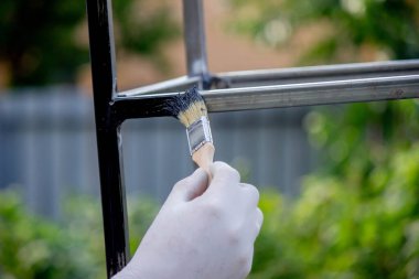 Bir adam metali siyah boyayla fırçayla boyuyor. Seçici odak