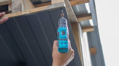 Bir adam çatıyı tamir eder, tornavidayla vidayı sıkar. Seçici odak