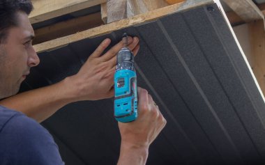 Bir adam çatıyı tamir eder, tornavidayla vidayı sıkar. Seçici odak