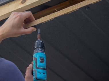 Bir adam çatıyı tamir eder, tornavidayla vidayı sıkar. Seçici odak