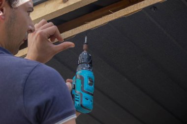 Bir adam çatıyı tamir eder, tornavidayla vidayı sıkar. Seçici odak