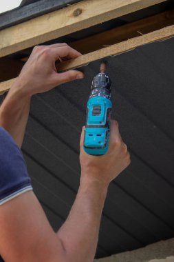 Bir adam çatıyı tamir eder, tornavidayla vidayı sıkar. Seçici odak