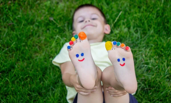 Ένα Αγόρι Στο Γρασίδι Ένα Ζωγραφισμένο Χαμόγελο Στα Πόδια Του — Φωτογραφία Αρχείου