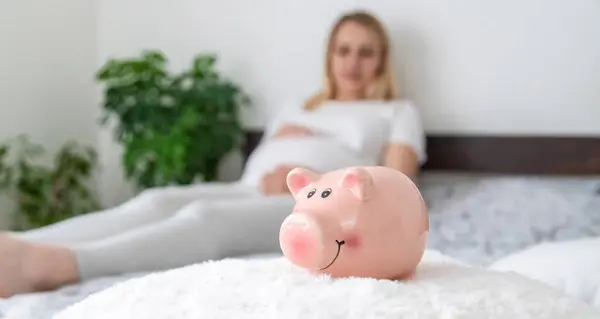 A pregnant woman holds a pig bank in her hands. Selective focus. People.