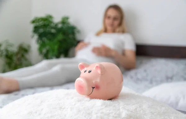 A pregnant woman holds a pig bank in her hands. Selective focus. People.