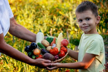 Bir kadın ve bir çocuk taze toplanmış organik sebzelerle dolu bir sepet tutuyorlar. Seçici odak