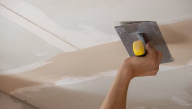 Adamın biri alçıdan tavana macun koyuyor. Plasterboard çarşafları için macun. Seçici odak
