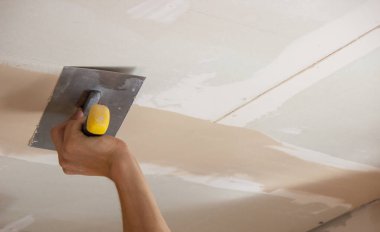 Adamın biri alçıdan tavana macun koyuyor. Plasterboard çarşafları için macun. Seçici odak