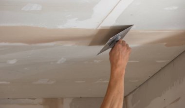 Adamın biri alçıdan tavana macun koyuyor. Plasterboard çarşafları için macun. Seçici odak