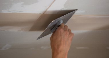 Adamın biri alçıdan tavana macun koyuyor. Plasterboard çarşafları için macun. Seçici odak