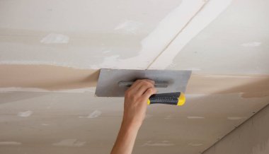 Adamın biri alçıdan tavana macun koyuyor. Plasterboard çarşafları için macun. Seçici odak
