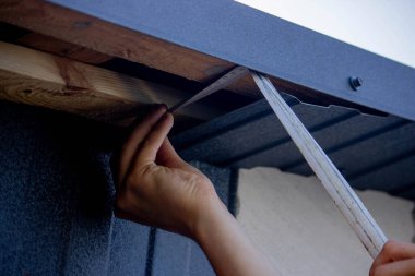 Bir adam çatıyı tamir eder, tornavidayla vidayı sıkar. Seçici odak