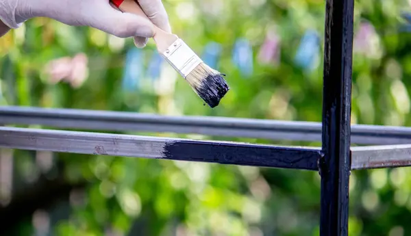 a man paints metal with black paint with a brush. Selective focus