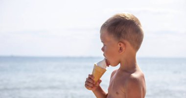 Küçük çocuk tatilde sahilde dondurma yiyor. deniz
