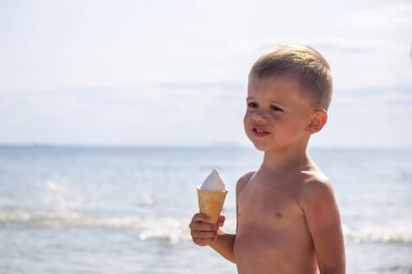 Küçük çocuk tatilde sahilde dondurma yiyor. deniz