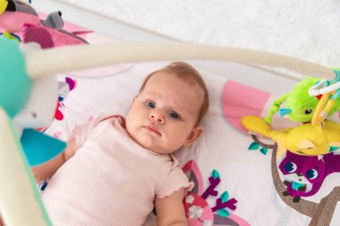 Bir bebek oyun hasırına asılı oyuncaklarla oynar. Bir çocuk, bir bebek evde oynuyor..