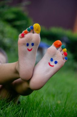 Boyalardan yapılmış bir deseni olan çocukların bacakları yeşil çimlerin üzerinde gülümsüyor..