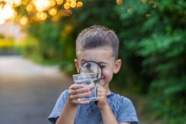 Bir çocuk, doğanın arka planına karşı büyüteçle suya bakar..