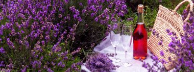 Lavanta tarlasında iki bardak ve pembe şarap. Arka planda mor çiçekler.
