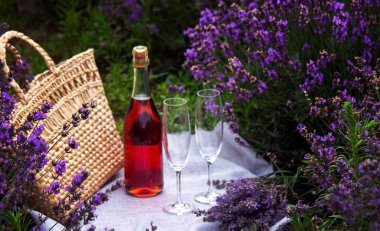 Lavanta tarlasında iki bardak ve pembe şarap. Arka planda mor çiçekler.