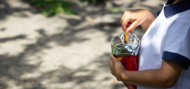 Bir çocuk doğanın arka planındaki bir paketten cips yer.