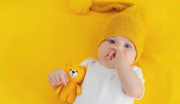 smiling baby girl goes to sleep with a teddy bear on a yellow background. children