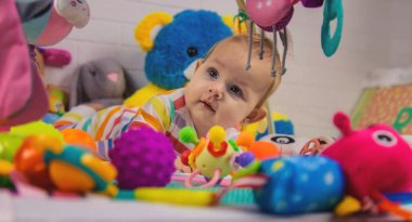 Bir çocuk oyun hasırına asılı oyuncaklarla oynar. Çocuk evde oyuncaklarla oynuyor.