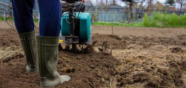 Erkek bir çiftçi tarlada bir traktörün arkasında yürüyor, tarlayı sabanla sürüyor..
