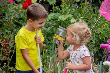 İki mutlu çocuk kelebekleri yakalar ve hayranlık duyar.