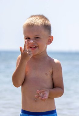 Çocuk kendine güneş kremi sürüyor. Güneşten korunma