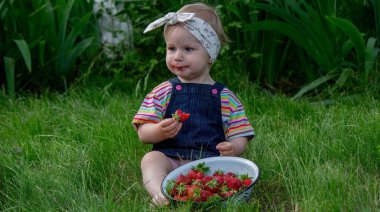 Küçük kız bahçede çilek yiyor. Seçici odak.