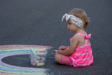 Küçük bir kız asfalta tebeşirle gökkuşağı çiziyor. Seçici odak.