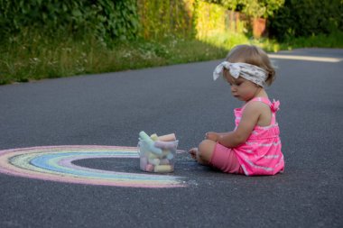 Küçük bir kız asfalta tebeşirle gökkuşağı çiziyor. Seçici odak.