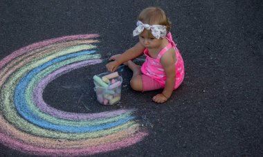 Küçük bir kız asfalta tebeşirle gökkuşağı çiziyor. Seçici odak.