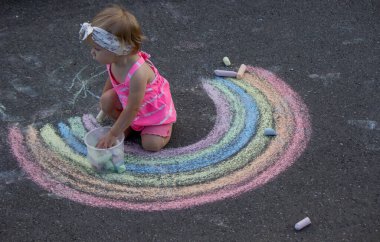 Küçük bir kız asfalta tebeşirle gökkuşağı çiziyor. Seçici odak.