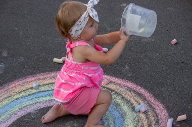 Küçük bir kız asfalta tebeşirle gökkuşağı çiziyor. Seçici odak.
