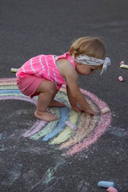 Küçük bir kız asfalta tebeşirle gökkuşağı çiziyor. Seçici odak.