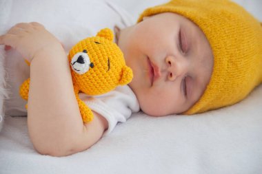 Yeni doğmuş bir bebek beyaz bir arka planda uyuyor, sarı bir ayıya sarılıyor..