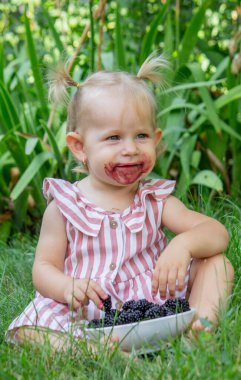 Küçük kız doğanın arka planında böğürtlen yiyor. Seçici odak.