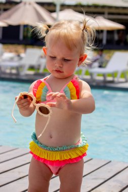 Havuzun arka planında güzel bir mayo ve güneş gözlüğü takan küçük bir kız. dinlenme