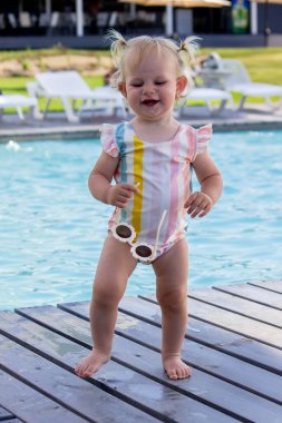 Havuzun arka planında güzel bir mayo ve güneş gözlüğü takan küçük bir kız. dinlenme