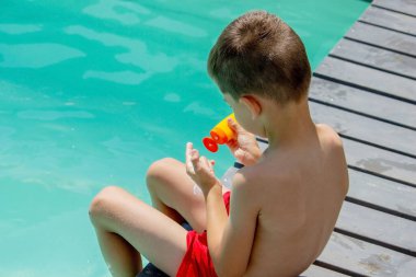 Bir çocuk yüzme havuzunun arka planına güneş kremi sürer. Güneşten korunma