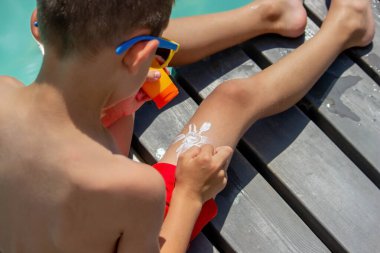Bir çocuk yüzme havuzunun arka planına güneş kremi sürer. Güneşten korunma