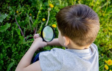 Çocuk büyüteçten çiçeğe bakıyor.