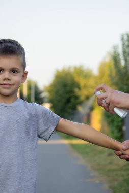 Kadın parkta, oğlunun eline böcek kovucu sürmüş. Yakın plan. Isırık önleyici.