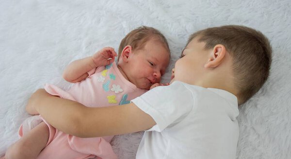 Брат целует младшую сестру. Старший брат и новорожденная девочка