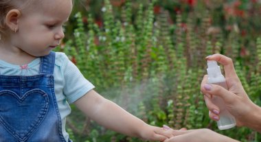 Anne çocuğun vücuduna sprey sprey sıkar. Seçici odak.